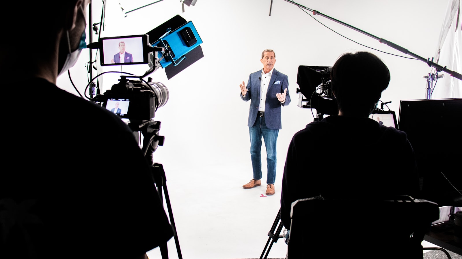 A presenter delivering to camera on a professional studio set, framed by production cameras and monitors — what a produced AI avatar spokesperson video looks like, beyond a plain talking-head tool demo.