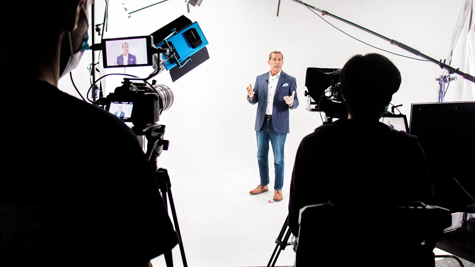A presenter delivering to camera on a professional studio set, framed by production cameras and monitors — what a produced AI avatar spokesperson video looks like, beyond a plain talking-head tool demo.