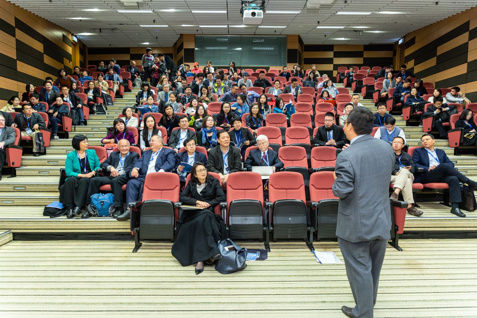 Conference keynote speaker addressing a seated auditorium audience wearing event lanyards
