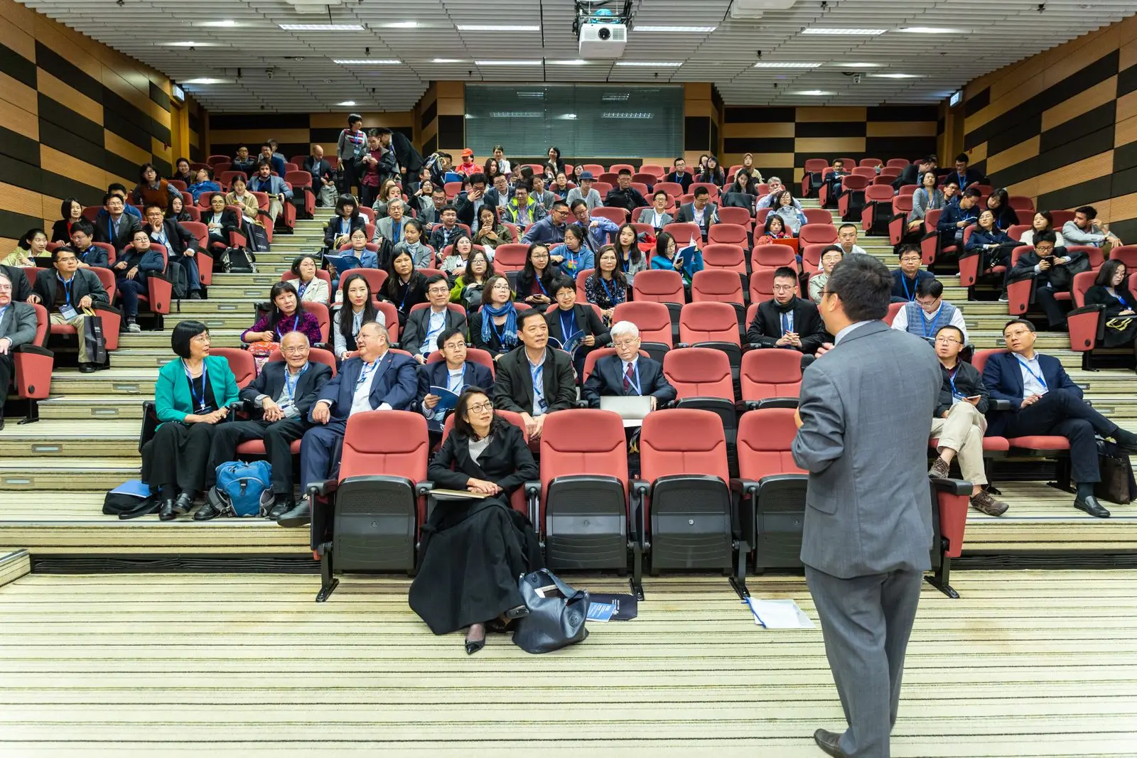 Conference keynote speaker addressing a seated auditorium audience wearing event lanyards